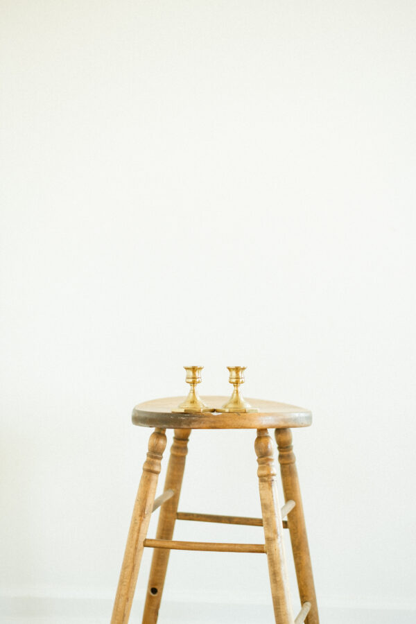 brass candlestick holders against white background on antique stool